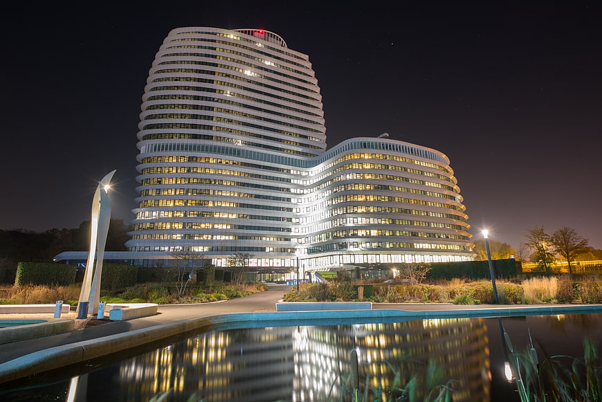 Modern curved office building illuminated at night with reflection