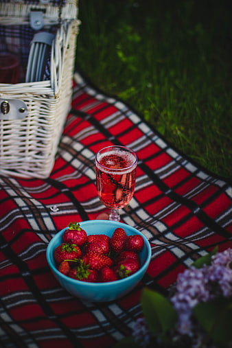 Summer picnic with strawberries, rosé wine, and wicker basket on plaid blanket
