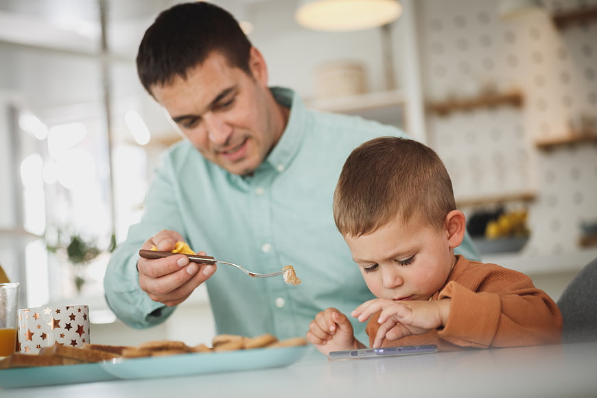 Father Feeding Reluctant Son at Breakfast Table