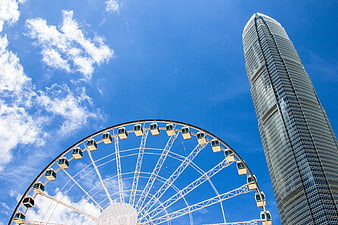 Low angle view of a Ferris wheel and skyscraper against a blue sky