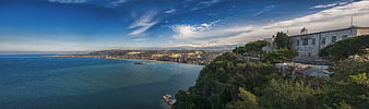 Panoramic coastal landscape with historic stone building and blue sea