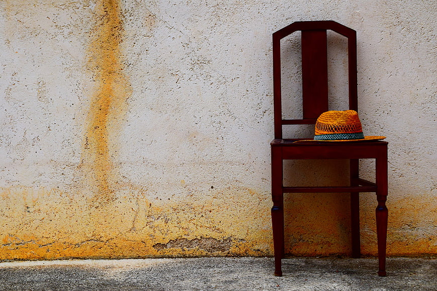Vintage wooden chair with orange hat against weathered Mediterranean wall