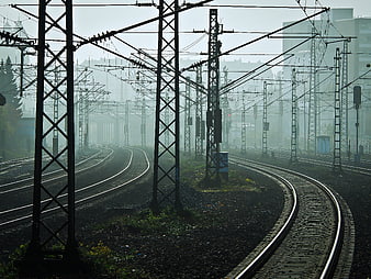 Foggy railway tracks with overhead catenary lines in urban setting