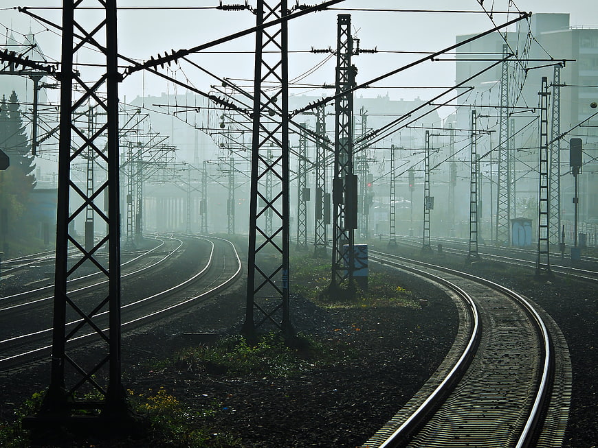 Foggy railway tracks with overhead catenary lines in urban setting