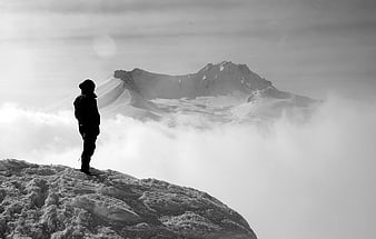 Silhouette of a mountaineer standing on a snowy peak above clouds