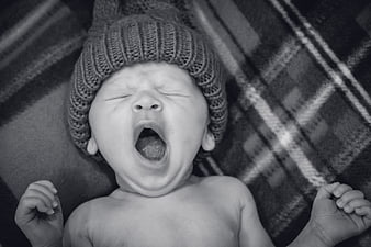 Black and white portrait of a yawning newborn baby wearing a knitted hat