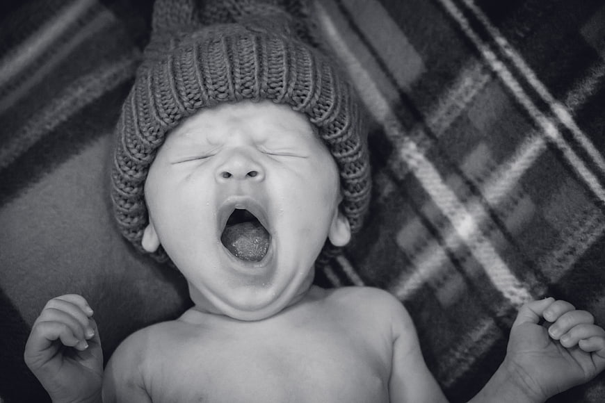 Black and white portrait of a yawning newborn baby wearing a knitted hat