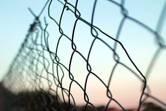 Close-up of chain-link fence against soft sunset sky