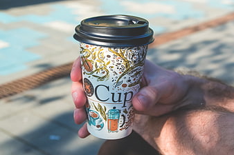 Hand holding illustrated coffee cup outdoors