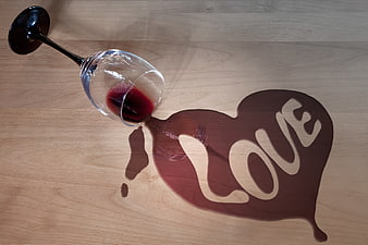 Red wine spilled into heart shape with love text on wood