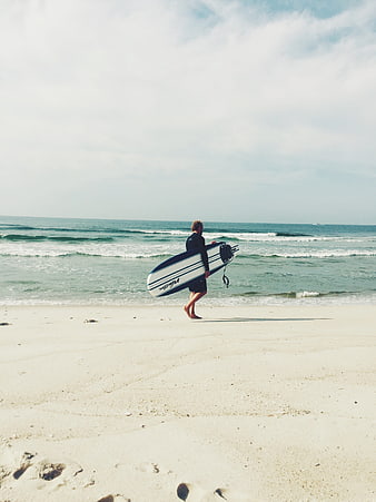 Surfer walking on sandy beach with surfboard