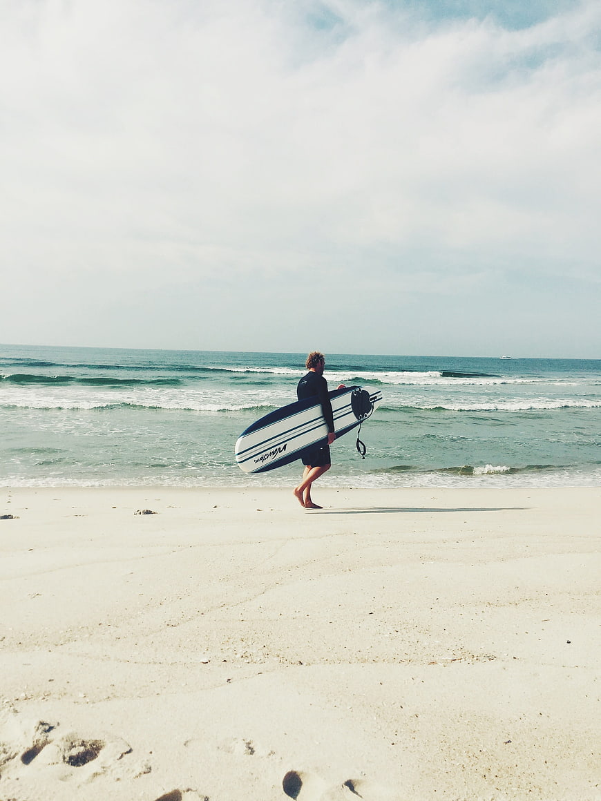 Surfer walking on sandy beach with surfboard
