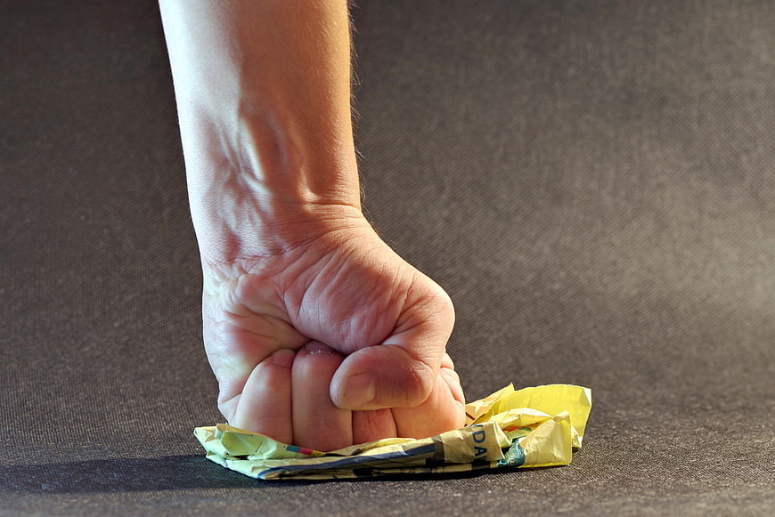 Hand Crushing Crumpled Paper on Dark Surface