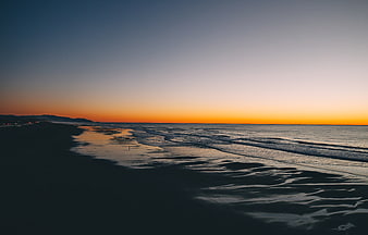 Serene Sunset Over Ocean Beach with Wet Sand Reflections