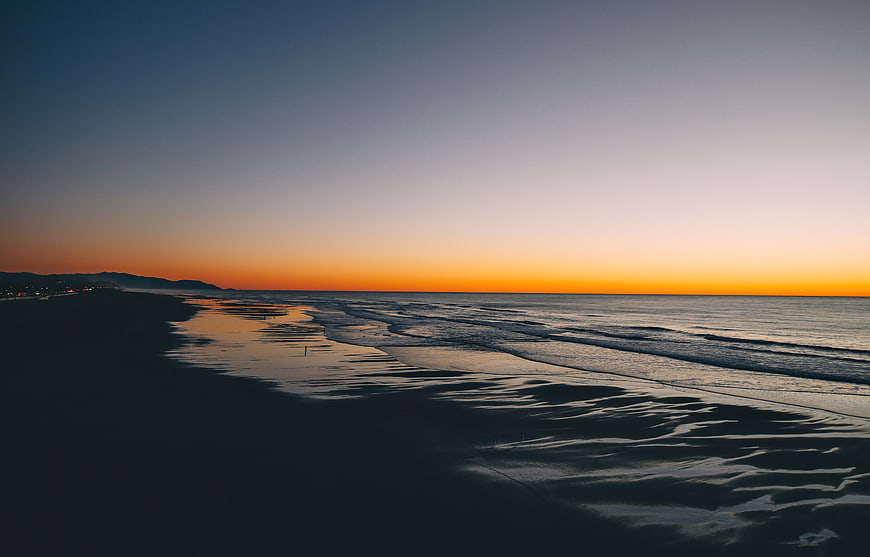 Serene Sunset Over Ocean Beach with Wet Sand Reflections