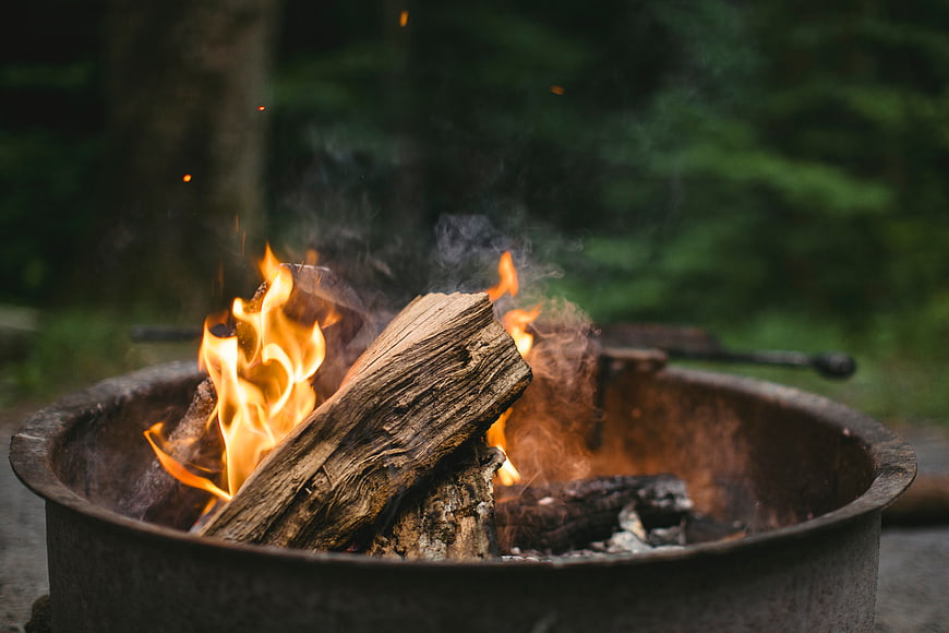 Campfire burning in metal fire pit with forest background