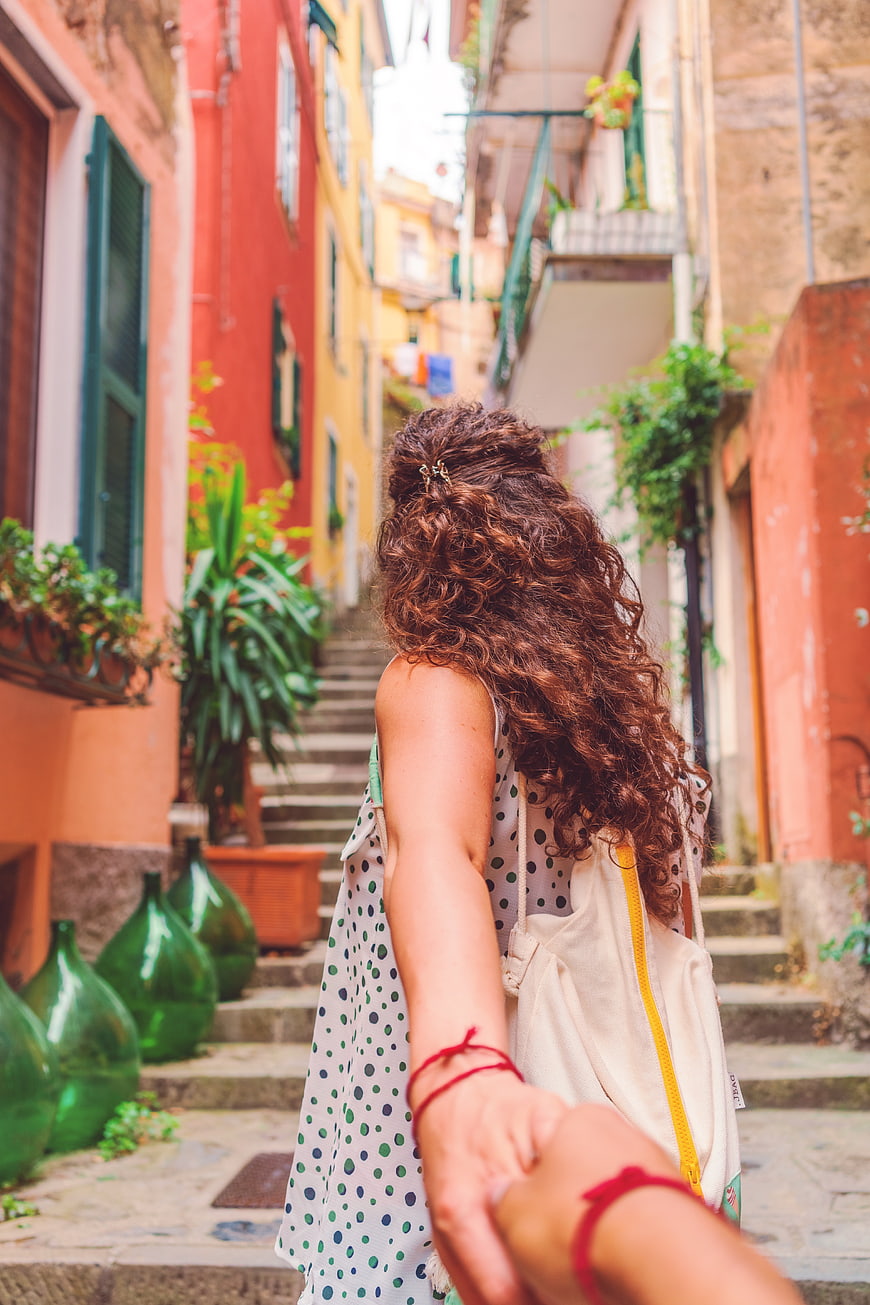 Woman with curly hair holding hands walking up colorful alley stairs
