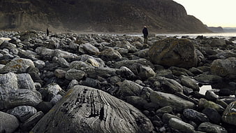 Man standing on rocky beach with mountain backdrop