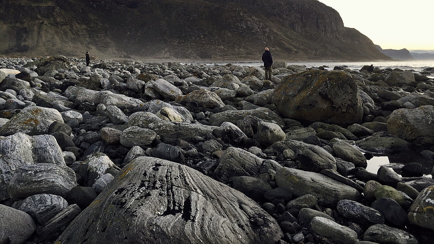 Man standing on rocky beach with mountain backdrop