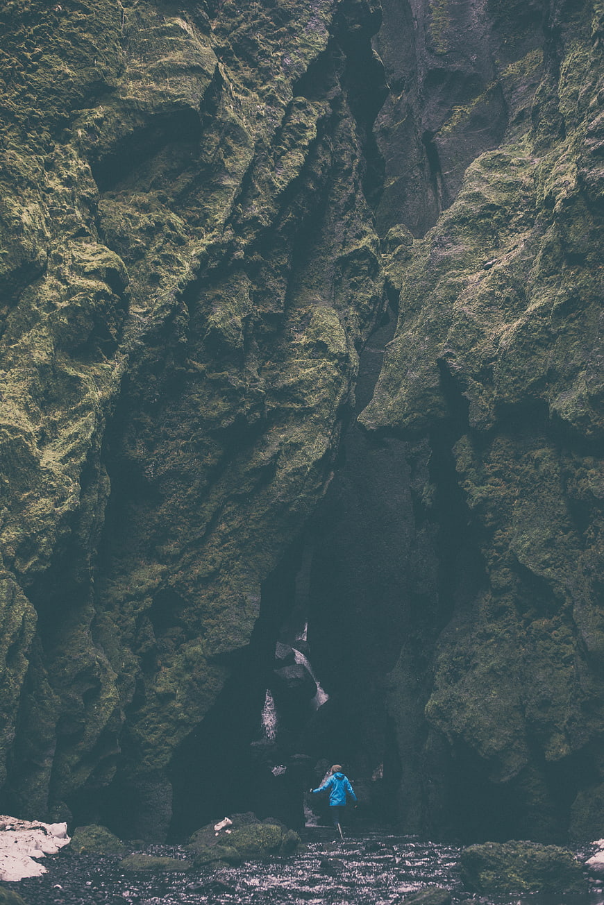 Woman in Blue Jacket Exploring Mossy Rock Cave