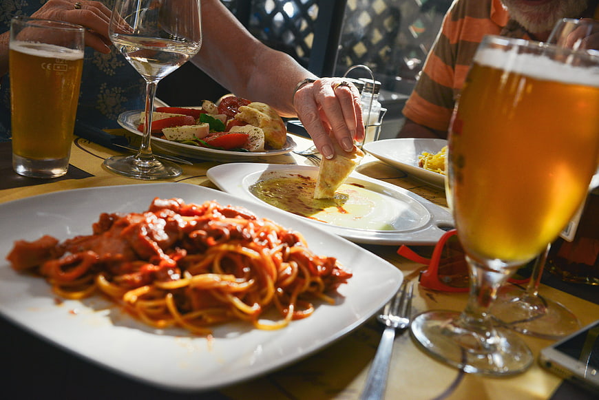 Friends enjoying Italian pasta and beer at a restaurant table