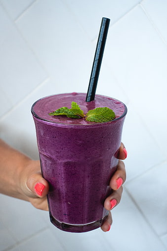 Hand holding purple smoothie with mint garnish