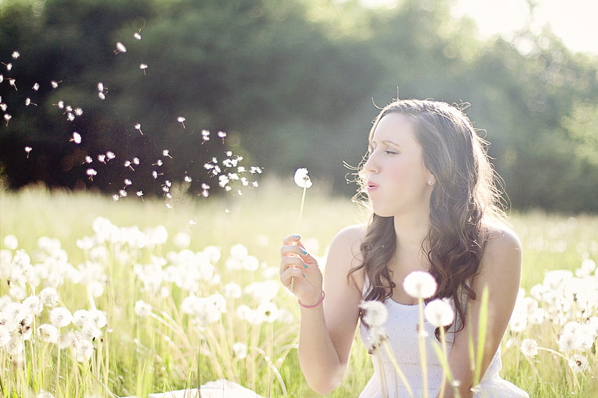Young woman blowing dandelion seeds in sunny meadow