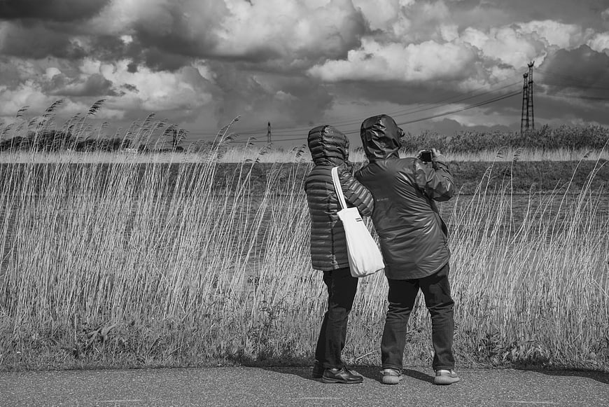 Two people in hooded jackets standing in windy field