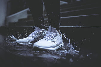 White sneakers splashing in water on dark stairs