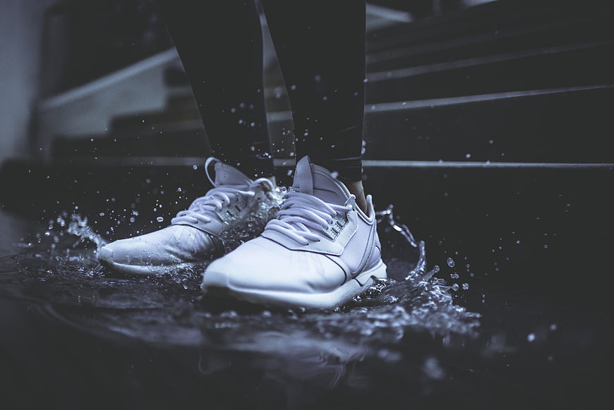 White sneakers splashing in water on dark stairs