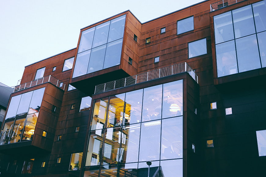 Modern rust-colored building with glass windows and warm interior lighting