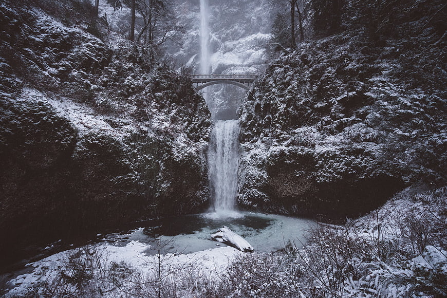 Snowy waterfall with bridge in winter forest landscape