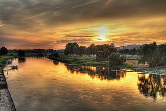 Golden sunset reflection on calm river with trees and sky