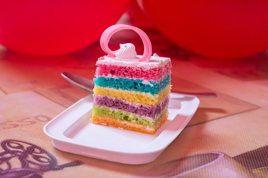 Colorful Rainbow Cake Slice on White Plate with Red Balloons