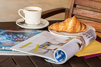 Croissant and coffee with magazine on wooden table