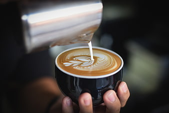 Barista Pouring Latte Art into Black Coffee Cup