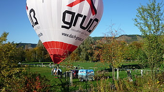 White and red hot air balloon landing on grassy field