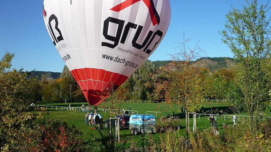 White and red hot air balloon landing on grassy field