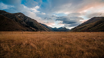 Golden grassy valley with mountains and dramatic sky