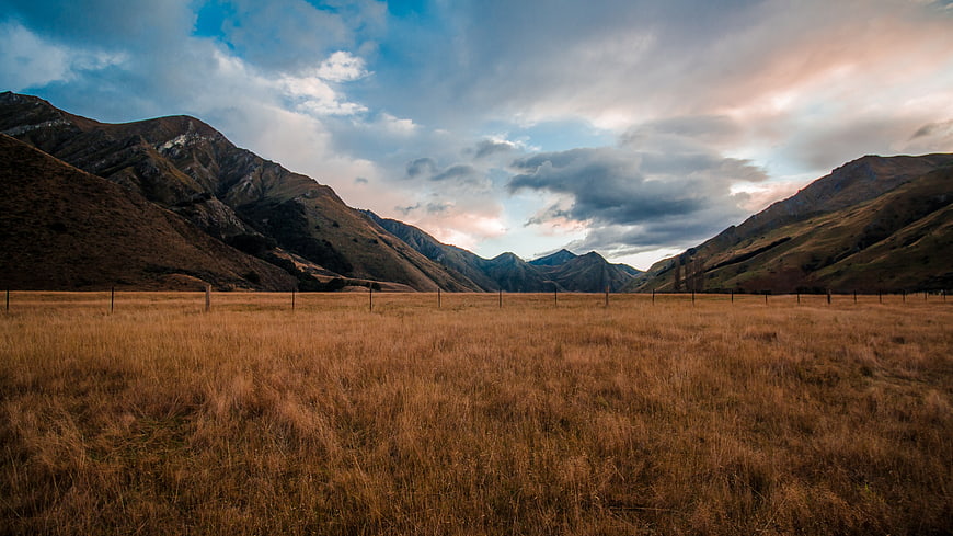 Golden grassy valley with mountains and dramatic sky