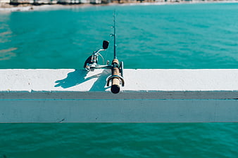 Fishing rod on white pier railing against turquoise ocean water