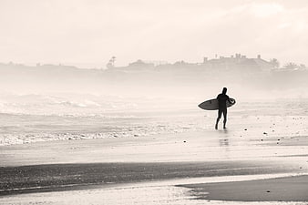 Surfer Silhouette Walking on Misty Beach with Surfboard