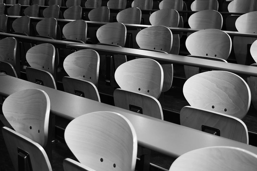 Black and white rows of empty wooden lecture hall seats