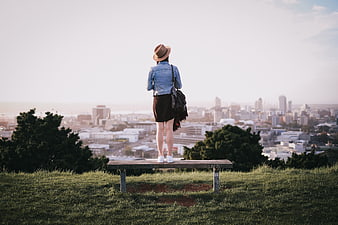Woman in Hat Standing on Bench Overlooking City Skyline