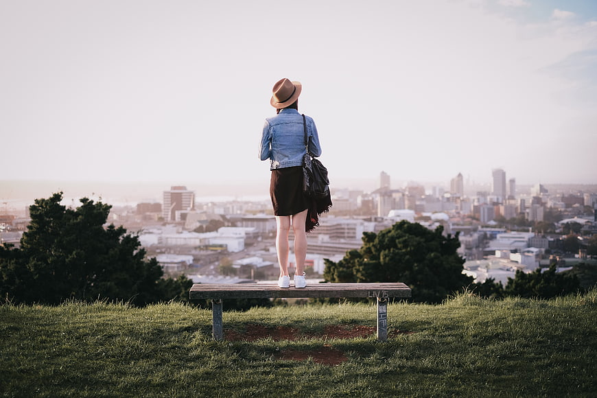 Woman in Hat Standing on Bench Overlooking City Skyline
