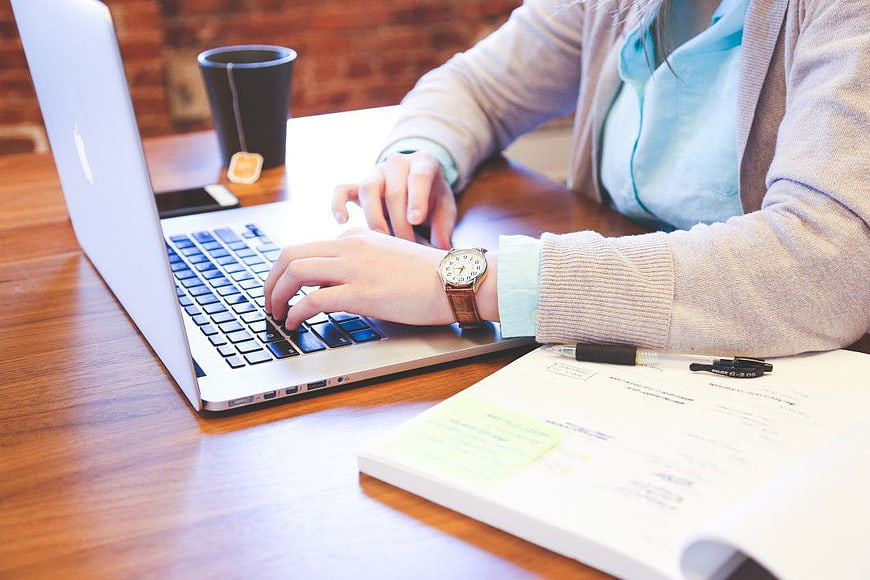 Woman Typing on Laptop with Notebook and Tea
