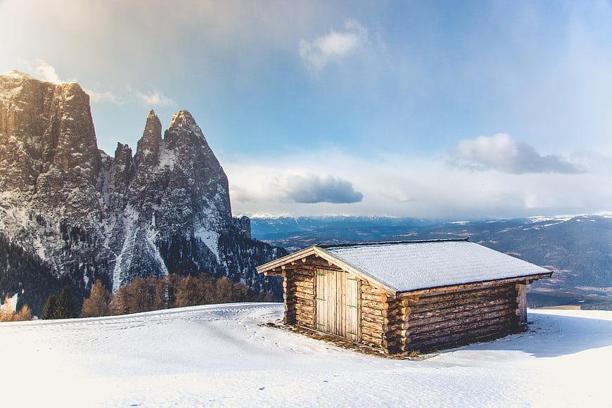 Rustic wooden cabin in snowy mountain landscape with peaks