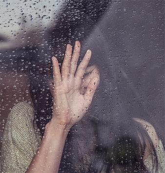 Woman's hand on rainy window glass with water droplets