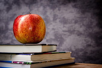 Red apple on stack of books against gray background