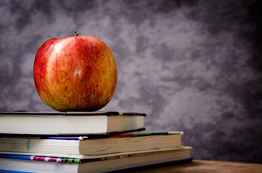 Red apple on stack of books against gray background